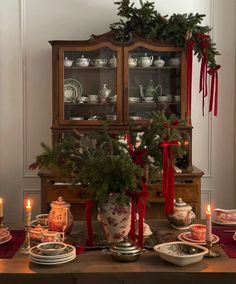 a dining room table with christmas decorations on it and candles in front of the china cabinet