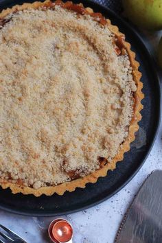 a pie sitting on top of a black plate next to an apple and silverware