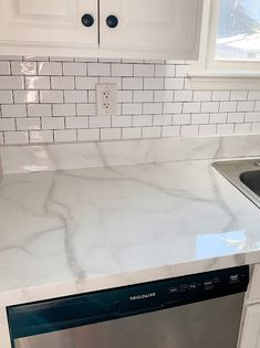 a white kitchen with marble counter tops and stainless steel dishwasher in the middle