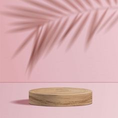 a round wooden base with a palm leaf shadow on the wall behind it, in front of a pink background