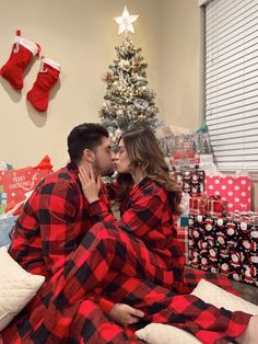 a man and woman sitting on a bed kissing in front of a christmas tree with presents