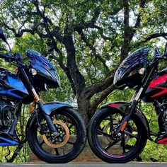 two motorcycles parked next to each other in front of a tree with leaves on it