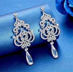 A beautiful pair of bridal earrings that is sure to make a bold statement on your Wedding Day! Adorned with glowing rhinestone crystals that capture the light from every angle with a perfectly translucent appeal, the earrings are silver plated for a bright finish which enhances the intricate detailing and conveys a modern take on old elegance. Overall length of the earring is 3.75" (approx. 9.5cm). Width: 1.25" (approx. 3.2cm). Weight: 23g. This exquisite design will add a touch of sophisticatio Silver Crystal Bridal Earrings For Glamorous Events, Silver Cubic Zirconia Earrings For Glamorous Events, Silver Drop Earrings For Glamorous Events, Silver Rhinestone Earrings For Glamorous Events, Silver Sparkling Earrings For Glamorous Events, Silver Earrings With Rhinestones For Glamorous Events, Sparkling Silver Earrings For Glamorous Events, Glamorous Silver Bridal Earrings With Rhinestones, Dazzling Silver Crystal Embellished Earrings