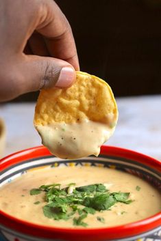 a hand holding a cracker over a bowl of soup