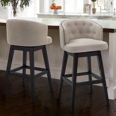 two white bar stools sitting next to each other in front of a kitchen counter