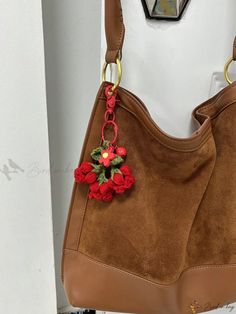 a brown purse with red flowers hanging from it's side and a gold ring around the strap