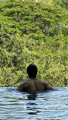 a man is swimming in the water with trees behind him and his back turned to the camera