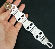 a hand holding a white crochet bracelet with a button on it's end