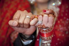 the bride and groom are holding hands with henna tattoos on their fingers while they hold each other's wedding rings