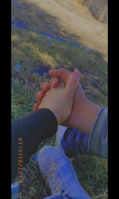 two people holding hands while sitting on the ground in front of some grass and dirt