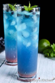 two glasses filled with blue liquid and mint sprinkled on the rim, sitting next to each other