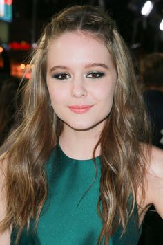 a young woman with long hair wearing a green dress and posing for the camera at an event