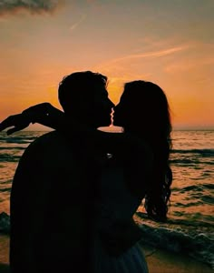 a man and woman are kissing on the beach at sunset, with their arms around each other