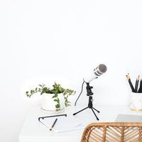 a white desk with a microphone, pen and notebooks on it next to a wicker chair