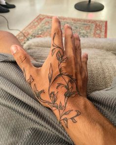 a man's hand with tattoos on it sitting on top of a couch next to a rug