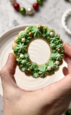 a person holding a decorated cookie in front of a plate with christmas decorations on it