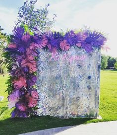 a purple and white wedding backdrop with flowers on the side, surrounded by greenery