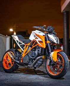 an orange and white motorcycle parked in front of a building at night with its lights on