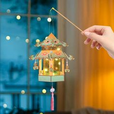 a person is holding a wind chime in front of a window with christmas lights