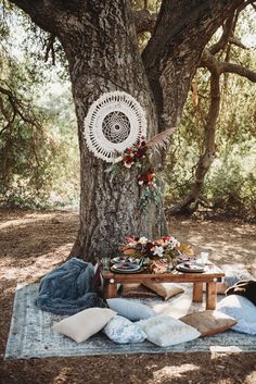 an outdoor picnic with blankets and pillows under a tree