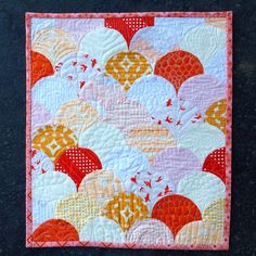 a quilted wall hanging on the side of a black surface with an orange and white design