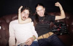 a man and woman sitting on top of a brown leather couch next to each other