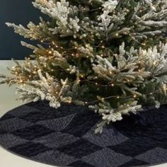 a small christmas tree in a black basket on top of a white tablecloth covered table