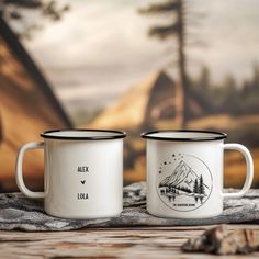 two coffee mugs sitting next to each other on top of a wooden table in front of a tent