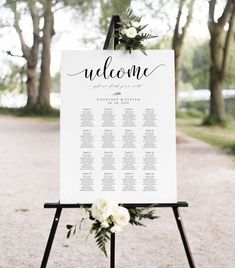 a seating sign with flowers on it and greenery around the table for an outdoor ceremony