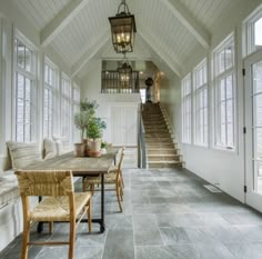 a dining room table and chairs in front of some windows with stairs leading up to the second floor