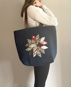 a woman is holding a black bag with flowers on the front and bottom, while standing against a wall