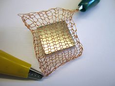 a pen is sitting next to a wire basket with a square shaped object inside it