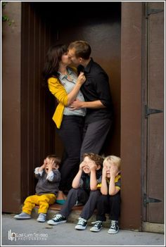 a man and woman kissing while two children sit on the ground next to each other