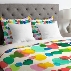 a bed with colorful polka dot sheets and pillows on top of it, next to a lamp