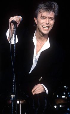 a man in black suit and white shirt holding a microphone with lights on the background