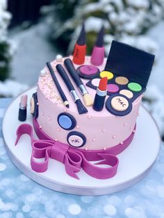 a pink cake with makeup and cosmetics on it sitting on a table in the snow