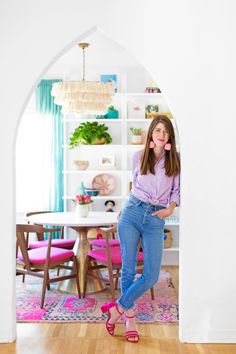 a woman standing in front of a dining room table with pink chairs and a white archway