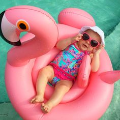 a baby wearing sunglasses sitting on an inflatable flamingo float