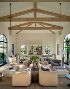 a living room filled with lots of furniture next to tall windows and wooden ceiling beams