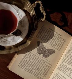 an open book sitting on top of a wooden table next to a cup of tea