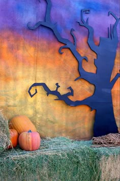 pumpkins and hay bales in front of a painted wall with a tree on it