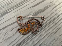 a brooch with an orange glass bead in the center on a wooden surface