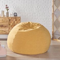 a yellow bean bag sitting on top of a hard wood floor next to a white brick wall