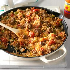 a skillet filled with rice and meat on top of a white counter next to a bottle