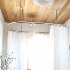 a white bed sitting under a wooden ceiling next to a window in a room with sheer curtains