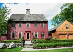 a red house with two lawn chairs in front of it and trees around the yard