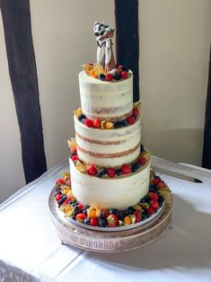 a three tiered cake with fruit on the side and a small figurine standing on top