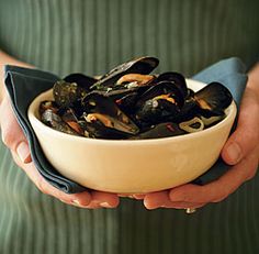 a person holding a bowl full of mussels in it's hands,