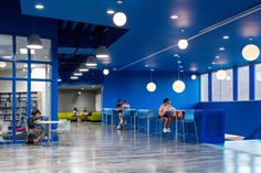 people sitting at tables in a library with bright blue walls and floor to ceiling windows