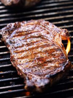 two steaks cooking on a grill with flames coming out of the top and one being grilled